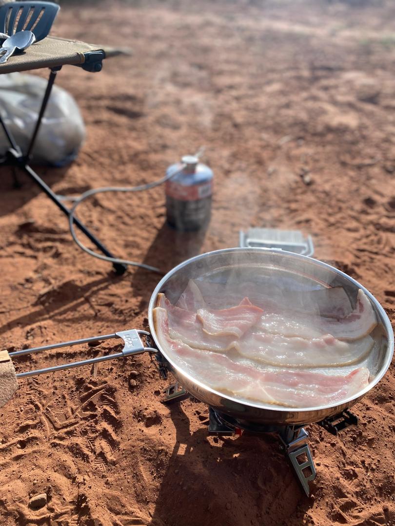 Bacon sizzling in a pan over an open fire