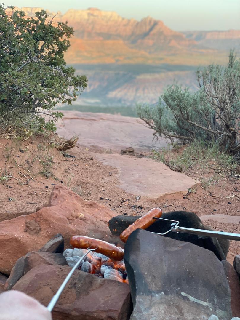 Grilling sausages over fire with canyon background