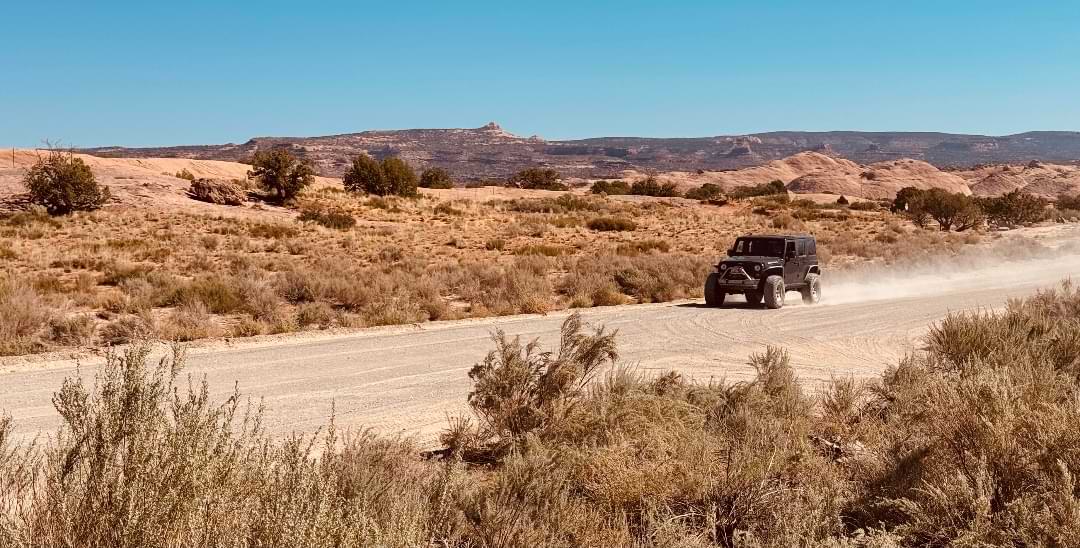 Black Jeep driving along a dusty road in the Utah desert