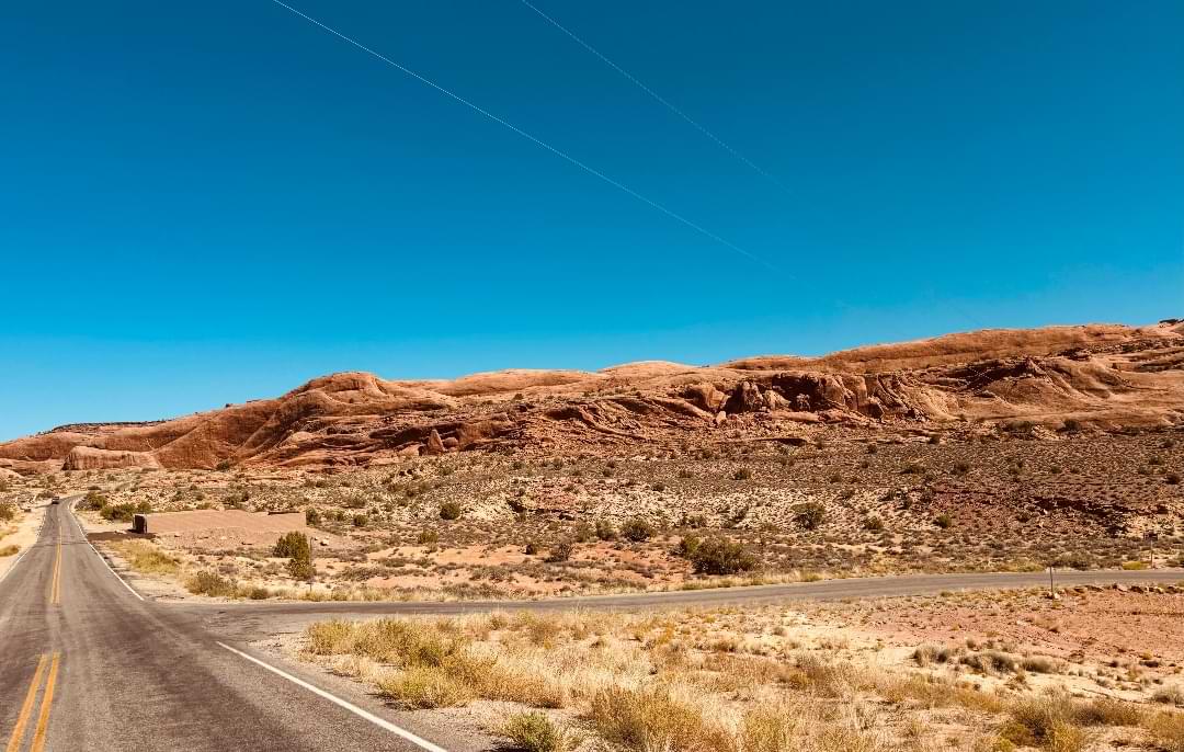 Open road through the Utah desert landscape with red rock hills under a clear blue sky