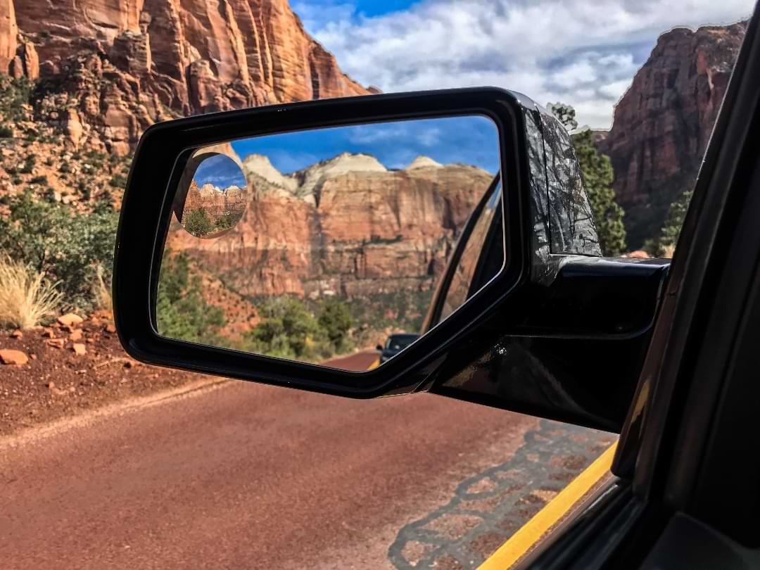 Reflections of Zion National Park cliffs in a car’s side mirror